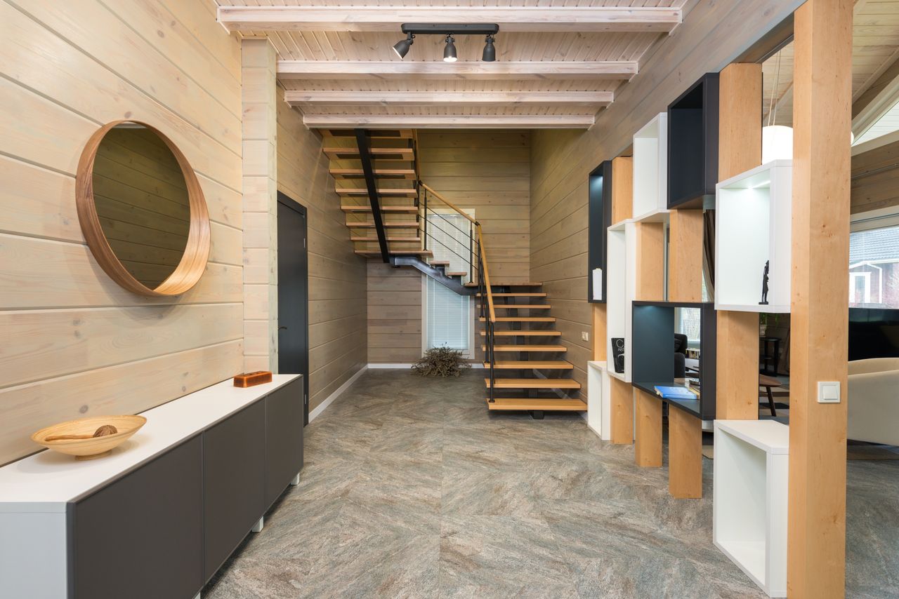 Interior of corridor with stairway and wooden geometric shelves opposite mirror hanging on wall above cupboard in stylish apartment